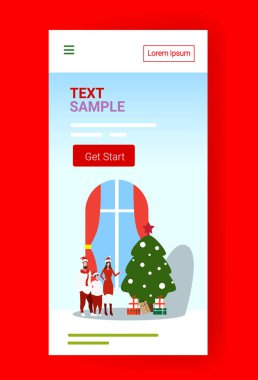 Noel Baba şapkalı mutlu aile Noel ağacının yanında duruyor yeni yıl kutlaması konsepti akıllı telefon ekranı çevrimiçi mobil uygulaması tam boy dikey