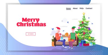 Elf şapkalı son sınıf öğrencisi olgun kadın ailesine hediye paketi veriyor. Kanepede oturmuş, mutlu yeni yıl tatillerini kutluyor. Kış tatili konsepti tam boy tebrik kartı yatay.