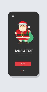Noel Baba, büyük çuval dolusu mutlu noeller ve kış tatilleri kutlaması konsepti akıllı telefon ekranı mobil uygulama fotokopi alanı ile duruyor.
