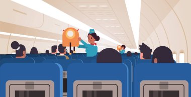 Hostes yolculara acil durumlarda ceket can yeleğinin nasıl kullanılacağını anlatıyor. Afro-Amerikan uçuş görevlileri güvenlik gösterimi konsepti modern uçak panosu iç yatay konsept