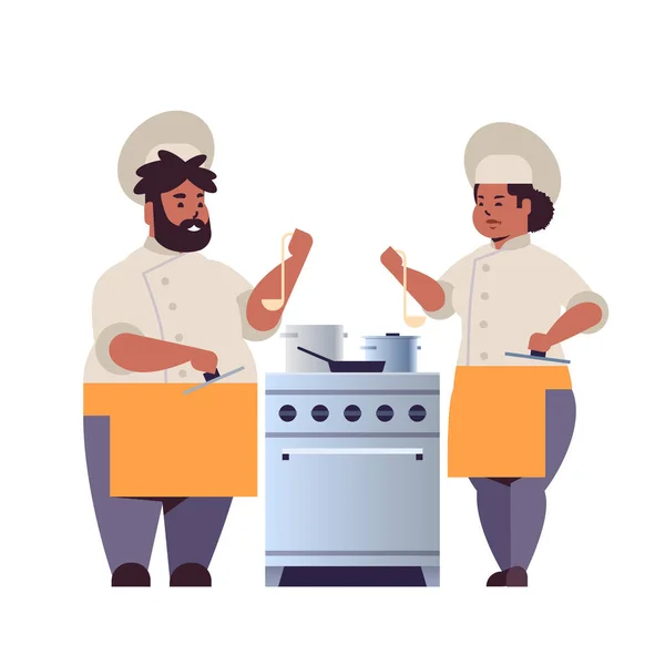 Cocina pareja de chefs profesionales preparando y degustando platos afroamericanos mujer hombre restaurante trabajadores en uniforme de pie juntos cerca de cocina estufa cocina concepto de comida plana de longitud completa — Archivo Imágenes Vectoriales