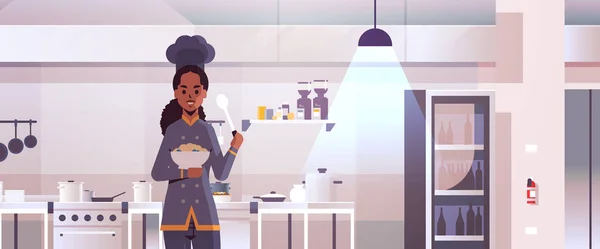 Cocinero profesional femenino plato de retención con gachas y cuchara mujer afroamericana en uniforme degustación plato cocina concepto de comida restaurante moderno cocina interior plano retrato horizontal — Archivo Imágenes Vectoriales