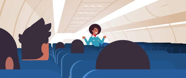 Stewardessa wyjaśniająca instrukcje dla pasażerów african American stewardessy w mundurze pokazującym wyjścia awaryjne koncepcja bezpieczeństwa pokładu samolotu w poziomie — Wektor stockowy