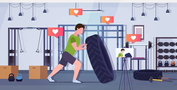 Fitness blogger flipping a tire trainer streaming ζωντανή εγγραφή βίντεο με κάμερα smartphone σε τρίποδο αθλητική δραστηριότητα προπόνηση blogging έννοια υγιεινού τρόπου ζωής γυμναστήριο εσωτερικό οριζόντιο πλήρες μήκος — Διανυσματικό Αρχείο