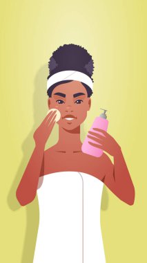 Afro-Amerikalı bir kız havluyla cildini temizliyor ve yüz bakımını yapıyor. Spa yüz bakımı konsepti portresi dikey.