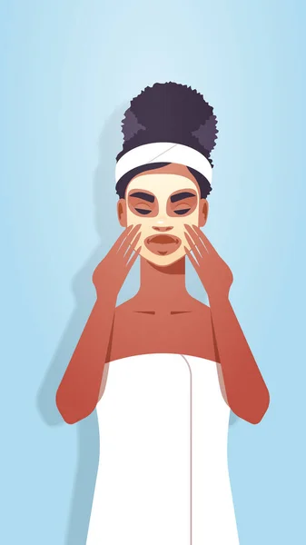 Mujer joven aplicando mascarilla vestida con toalla chica afroamericana con piel fresca limpia tratamiento facial spa tratamiento facial retrato vertical — Archivo Imágenes Vectoriales