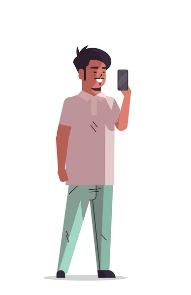 Hintli bir adam akıllı telefon kamerasında fotoğraf çekiyor. Gülümseyen erkek çizgi film karakteri dikey pozisyonda duruyor. — Stok Vektör