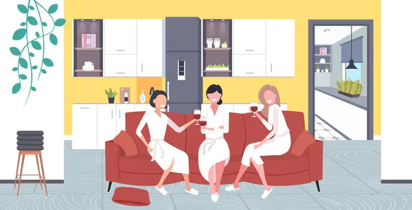 Hermosas mujeres en albornoces beber vino divertirse casa cuidado concepto niñas relajarse en el sofá — Vector de stock