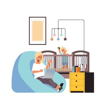 Evde dizüstü bilgisayar kullanan serbest çalışan meşgul bir anne. Küçük oğlu beşikte oyuncaklarla oynuyor.