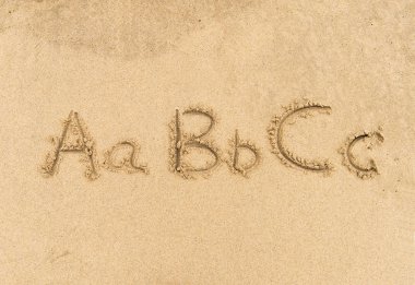 Alfabe harfleri kumsalda el yazısıyla yazılmış.