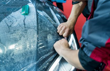 Worker spraying water onto car to install paint protection film clipart