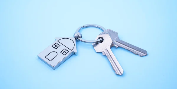 Přívěšek na klíče se symbolem domu a klávesami na modrém pozadí, Real est — Stock fotografie