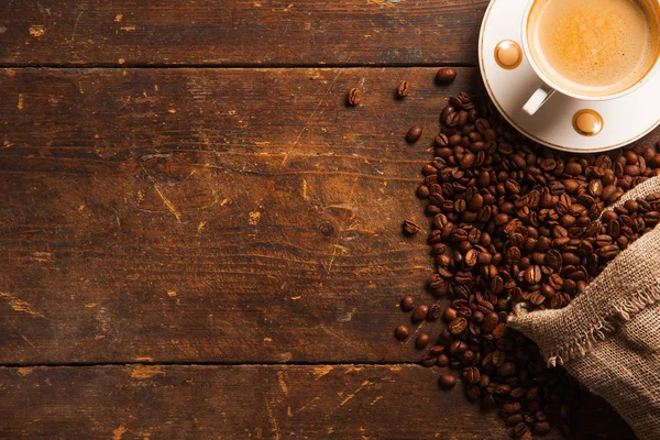Šálek kávy a fazole na dřevěném stole — Stock fotografie