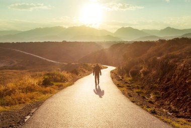 Dağlarda manzaralı bir yol. Seyahat geçmişi. Gündoğumu arka planında giden adam.