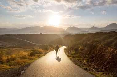 Dağlarda manzaralı bir yol. Seyahat geçmişi. Gündoğumu arka planında giden adam.