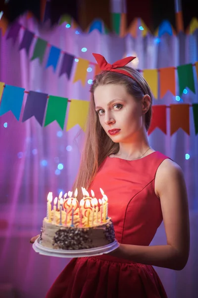 Beautiful young vintage pin up style girl standing in colorful lighted scene holding cake with candles.