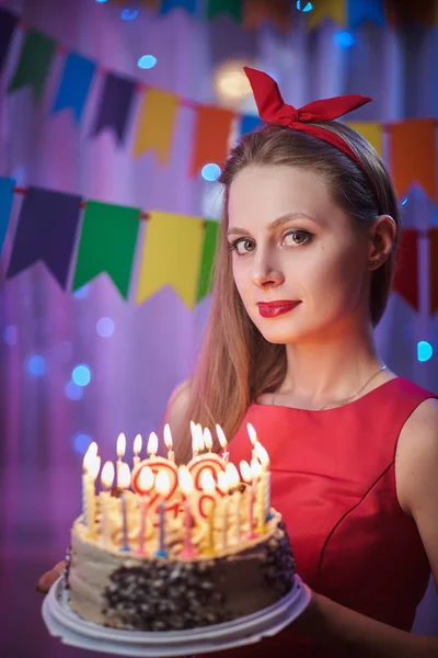 Piękne młode rocznika szałowy styl dziewczyna stojąc w kolorowe sceny oświetlone trzyma tort ze świecami. — Zdjęcie stockowe
