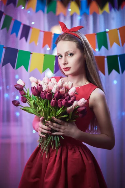 Hermosa joven vintage pin up chica de estilo de pie en colorida escena iluminada sosteniendo flores . —  Fotos de Stock