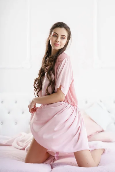 Красивая молодая женщина чувственно улыбается на кровати, играя с розовым набором пижамы — стоковое фото