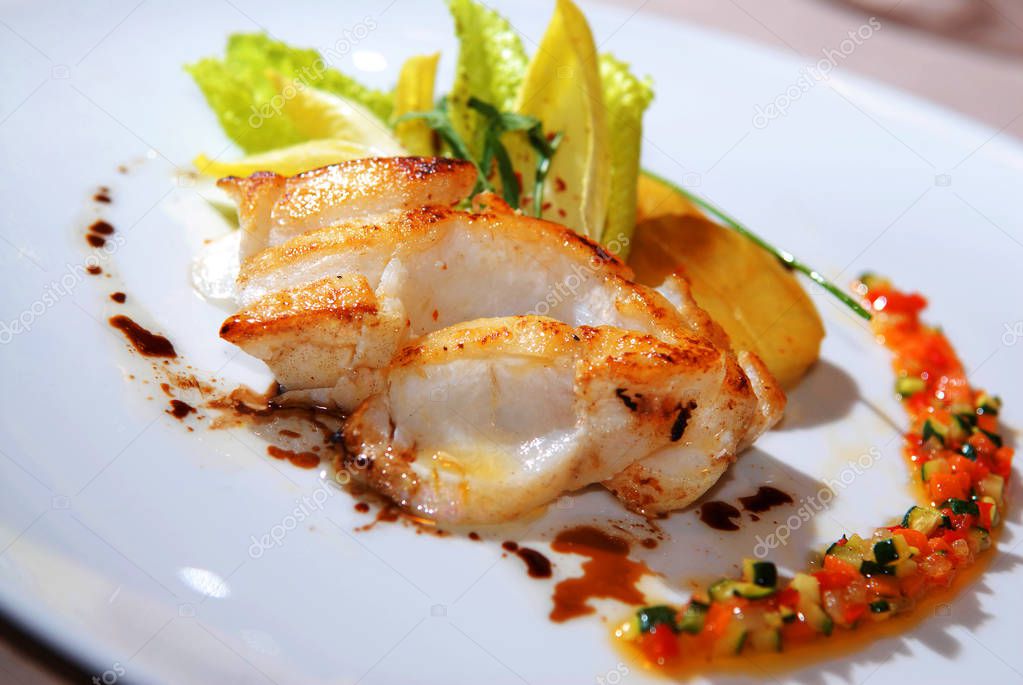 Fried cod fish fillet with lettuce and vegetable as close-up on 