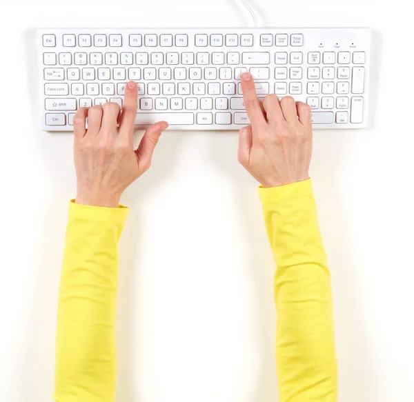 Mãos em casaco amarelo e teclado branco — Fotografia de Stock