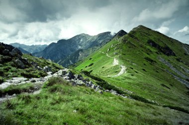 Yeşil dağlar ve karanlık bulutlu gökyüzü.