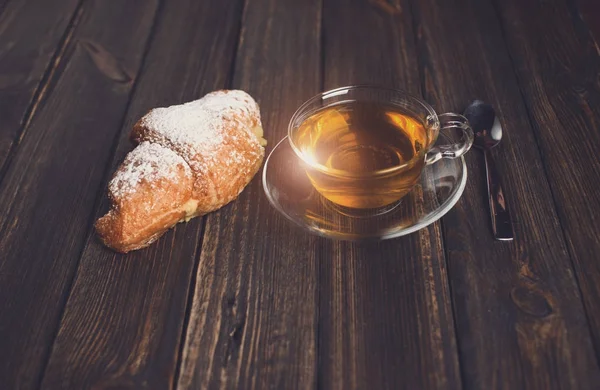 Круассан с чаем на деревянном столе — стоковое фото