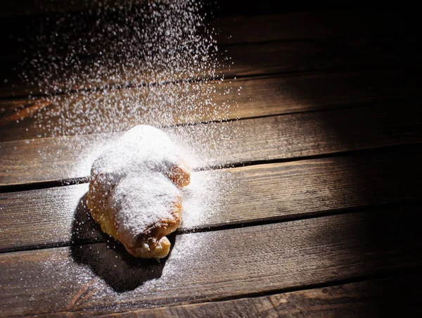 Croissant en escritorio de madera con azúcar en polvo que cae —  Fotos de Stock