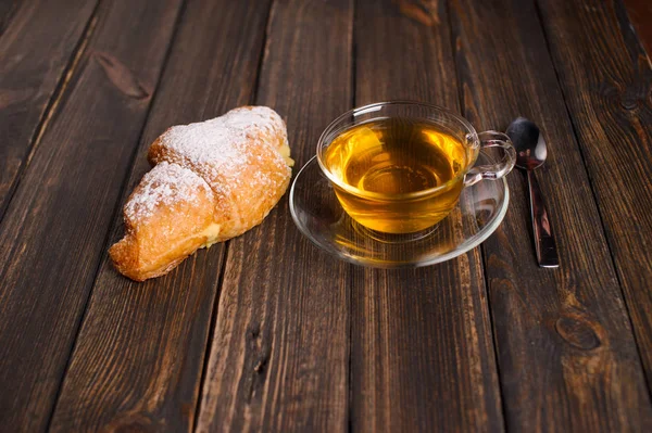 Круассан с чаем на деревянном столе — стоковое фото