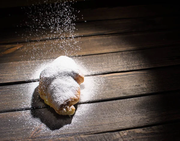 Croissant en escritorio de madera con azúcar en polvo que cae —  Fotos de Stock