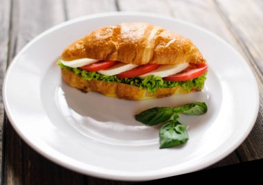 Koyu ahşap zemin üzerine jambon ve salata yaprağı taze kruvasan