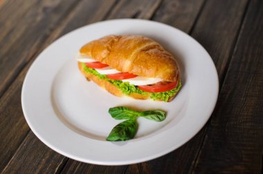 Koyu ahşap zemin üzerine jambon ve salata yaprağı taze kruvasan