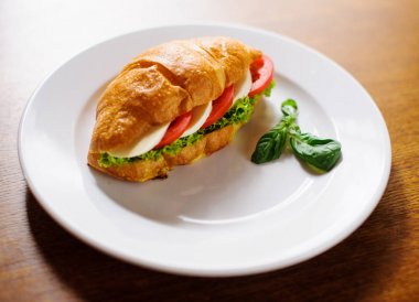 Koyu ahşap zemin üzerine jambon ve salata yaprağı taze kruvasan