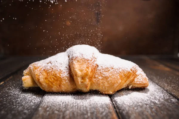 croissant with powdered sugar on wooden desk