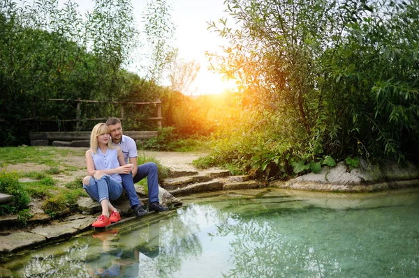 Láska pár sedí na skále u řeky a na západ slunce — Stock fotografie