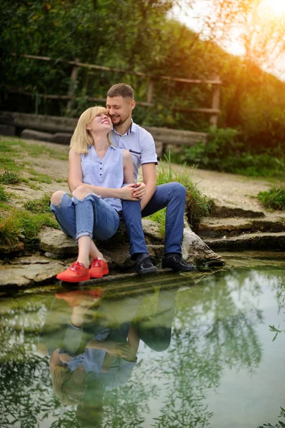 Miłość para siedzi na skale w rzece i widokiem na zachód słońca — Zdjęcie stockowe