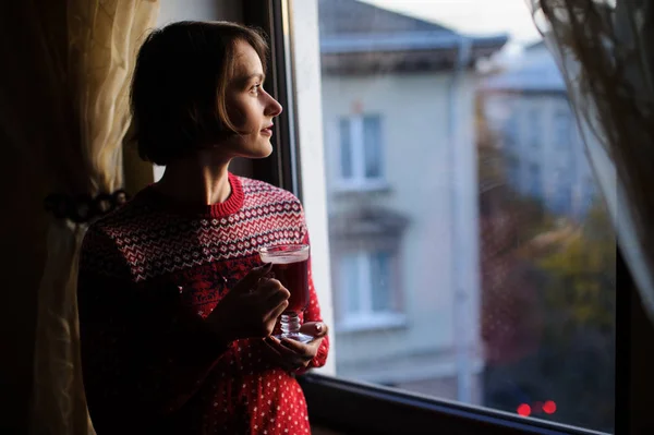 Woman holding a glass of mulled wine while looking out of the wi — Stock Photo, Image