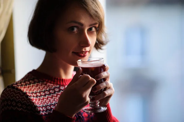Женщина держит стакан глинтвейна, глядя из wi — стоковое фото