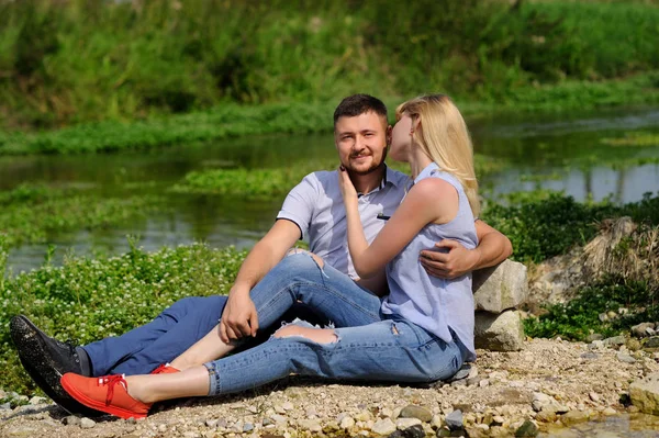 Láska pár sedí na skále u řeky a na západ slunce — Stock fotografie