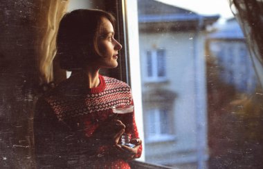 Bir pencere yanında duran, kırmızı kış giysileri giyiyor ve içme güzel kadın mulled şarap