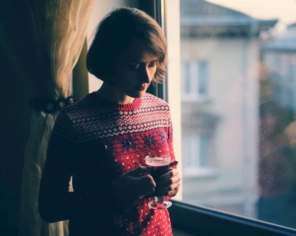 Bir pencere yanında duran, kırmızı kış giysileri giyiyor ve içme güzel kadın mulled şarap