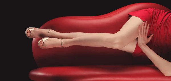 在黑色背景上的红色沙发上的银鞋的女人腿 — 图库照片