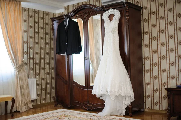 美しくエレガントな白いウェディングドレスと結婚式のお祝いを期待してワードローブにぶら下がっている男性新郎新婦のウェディングスイート — ストック写真