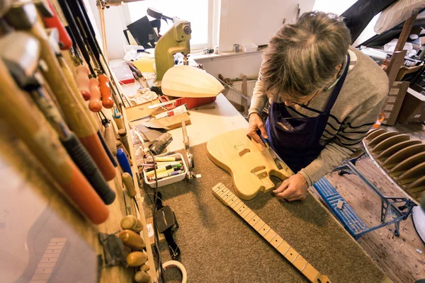 Guitar repairer clearing the sawdust from an electric guitar — Stock Photo, Image