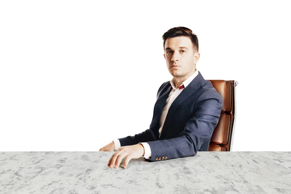 Привлекательный бизнесмен в модном костюме сидит за столом на пустом фоне — стоковое фото