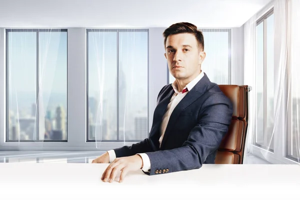 Atraktivní podnikatel s moderní oblek sedí proti moderní kancelářské zobrazení — Stock fotografie