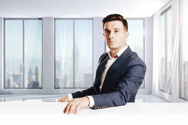 Aantrekkelijke zakenman met moderne pak zitten tegen moderne kantoor weergave — Stockfoto