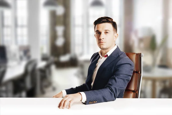 Привабливий бізнесмен з сучасним костюмом, що сидить на тлі сучасного вигляду офісу — стокове фото