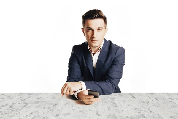 Привлекательный бизнесмен в модном костюме сидит за столом на пустом фоне — стоковое фото