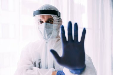 Erkek doktor ya da bilim adamı koruyucu giysi giyiyor ve yüz maskesi, dur, el hareketi.